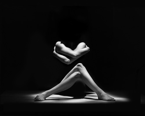 Nude arms and legs emerging from darkness